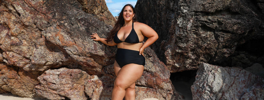 Woman with long brown hair wears black triangle bikini top and high waisted full coverage black bikini bottoms