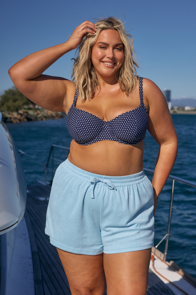 Model wearing light blue shorts and navy dots bikini top on boat