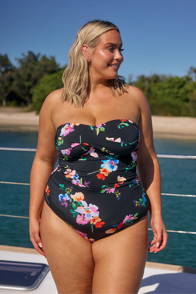 Model wearing black floral strapless one piece on boat