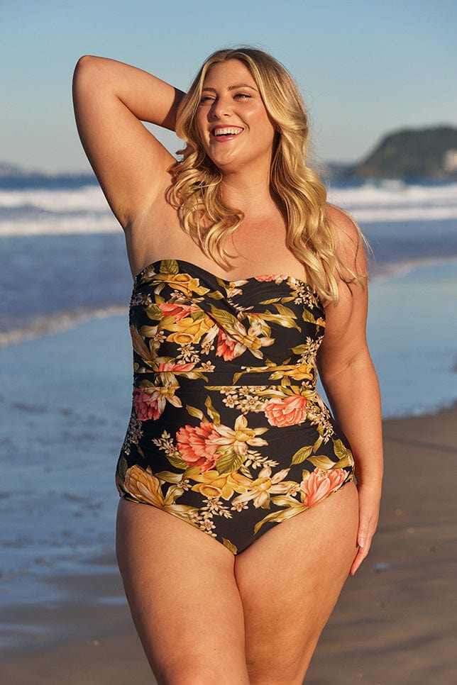 model wearing a strapless one piece swimsuit with yellow and orange flowers at beach