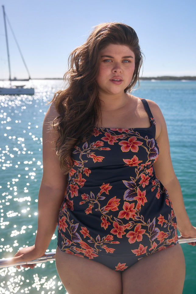 Brunette model wearing navy and orange floral tankini and pant on boat