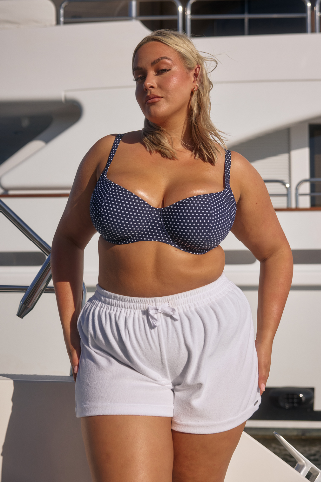 Model wearing white shorts with navy and white dots bikini top