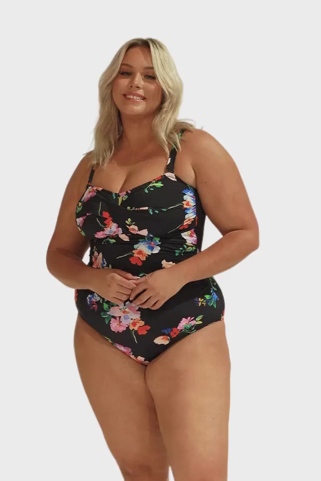 Model wearing black floral twist front bandeau one piece swimsuit